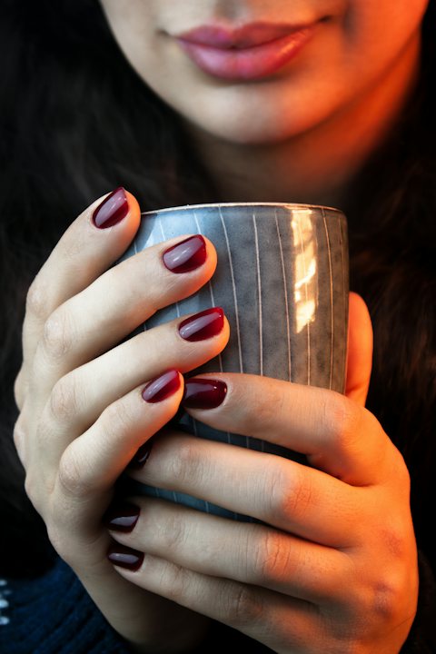 Dark burgundy nails holding a cozy mug