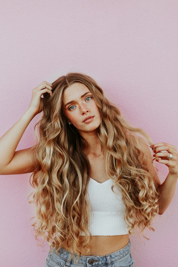 Woman with long voluminous wavy hair against a blush pink background